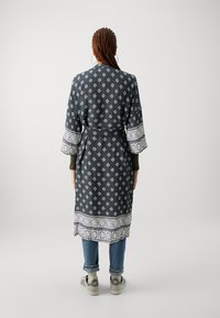 Dlhý, tmavomodrý župan v štýle kimono s bielymi diamantovými a geometrickými vzormi, širokými rukávmi a dekoračným lemom. Zaviazaný v páse.