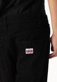 Pantaloni in denim neri con una tasca posteriore decorata con un'etichetta rossa e bianca "ONLY & SONS". Il tessuto ha una texture liscia con cuciture visibili.