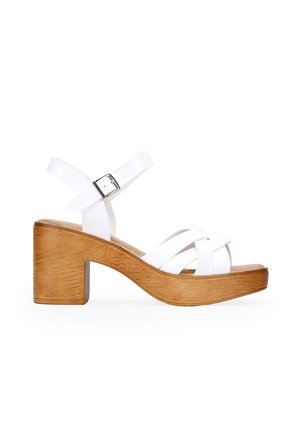 Sandales à talons en cuir blanc avec un talon en bois, des lanières entrecroisées et une boucle réglable à la cheville. Texture lisse, design à bout ouvert.