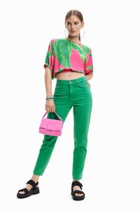 Beskaaret pink top med grønt bladmønster, grønne tætsiddende jeans og sorte sandaler. Modellen holder en lille pink håndtaske.