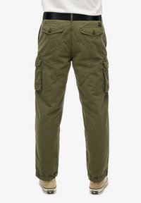 Pantaloni cargo verde oliva con gamba affusolata, polsini elastici, tasche laterali e tasche posteriori con chiusura a bottone. Tessuto resistente.
