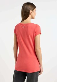 T-shirt in cotone corallo con maniche corte arrotolate e scollatura rotonda. Un bottone rotondo in argento si trova sulla parte superiore della schiena.