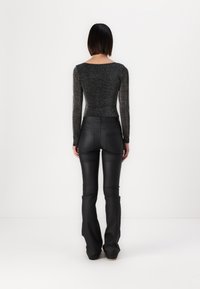 Haut noir à manches longues en tissu texturé et brillant, associé à un pantalon en cuir noir ajusté, avec des jambes évasées et une finition lisse.