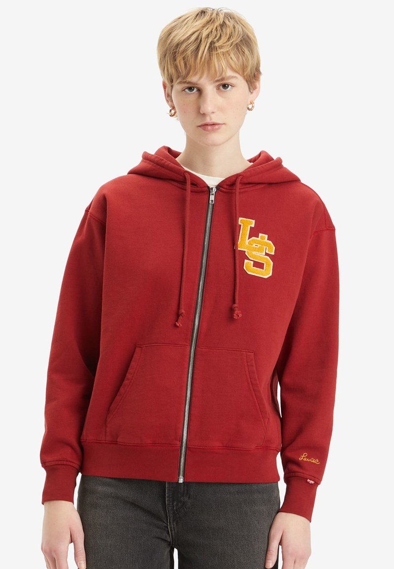 Hoodie rouge zippé fabriqué en tissu doux, avec une poche avant, une capuche avec cordon de serrage et un logo "LS" brodé en jaune.