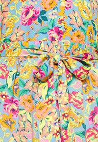 Tecido com padrão floral em cores pastel, apresenta grandes flores rosas e amarelas sobre um fundo azul claro, com um detalhe de cintura amarrada.
