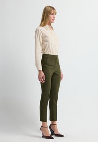 Beige overhemd met kraag en knopen, gecombineerd met hooggetailleerde, donkergroene taps toelopende broek en bordeauxrode hakken, met strakke lijnen en een getailleerde pasvorm.