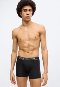Μαύρα ανδρικά εσώρουχα boxer από βαμβάκι, με μέση που φέρει το λογότυπο "TOMMY HILFIGER" σε λευκό χρώμα. Σχεδίαση που εφαρμόζει στενά και λεία υφή.