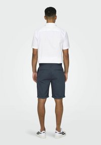 Chemise blanche à manches courtes et short bleu foncé avec revers, vue de dos. Le short comprend deux poches arrière et une finition texturée.