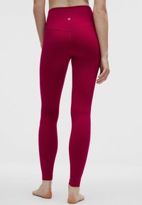 Felső derekú, testhezálló leggings, élénk magenta színben, rugalmas anyagból készült. Simább textúrával és minimális varrási részletekkel rendelkezik.