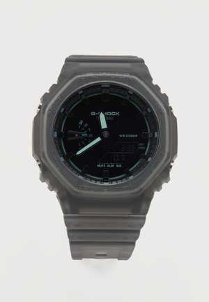 Črna ura Casio G-Shock z okroglo digitalno-analogno številčnico, prozornim nahrbtnim paščkom in indikatorji datuma ter časa na številčnici.