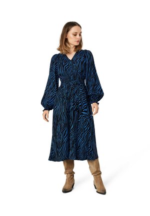 Langsleeve, blauw en zwart gestreepte jurk met een smocktail en V-hals ontwerp, gecombineerd met beige kniehoge laarzen.