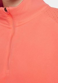 Sudadera de forro polar en color coral brillante con un collar de media cremallera, que presenta una textura suave y acentos punteados en los hombros.