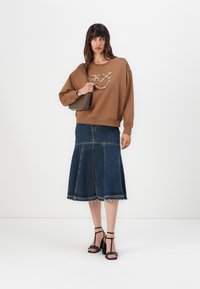 Bruine sweatshirt met een текстуур ontwerp, gecombineerd met een denim midi-rok met een split aan de voorkant. Zwarte strappy hakken accentueren de outfit.