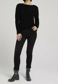 Czarny sweter dzianinowy z szerokim dekoltem, w połączeniu z czarnymi wąskimi dżinsami. Całość dopełniają czarne sznurowane buty bojowe.
