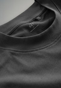 Close-up van de kraag van een zwart T-shirt met ronde hals die het gedrukte maatlabel M en de tekst "Made in Romania" aan de binnenkant toont.