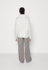 Lichtgrijze gebreide trui met een brede kraag en geribde zoom, gecombineerd met loszittende grijze cargobroek met zijzakken.
