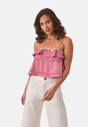 Top corto rosa con dobladillo con volantes, detalles de encaje y tirantes finos, combinado con pantalones cargo blancos con bolsillos y bordados sutiles.