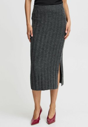 Grauer gerippter Strickrock mit einem seitlichen Schlitz, versehen mit einem eng anliegenden Taillenbund. Der Stoff wirkt weich mit einer strukturierten Oberfläche. Getragen mit roten High Heels.