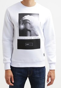 Weißes Sweatshirt mit einem großen Schwarz-Weiß-Grafikdruck, der einen Schornstein und Text zeigt. Mit gerippten Bündchen und Halsauschnitt, aus weichem Stoff.