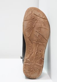 Sole of a black leather shoe with worn, tan rubber outsole showing textured patterns and visible wear marks.