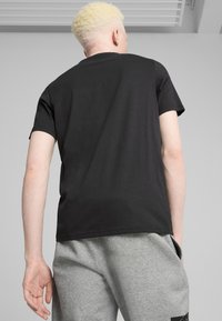 Sort bomulds T-shirt med korte ærmer og klassisk crew neck, set bagfra. Matchet med grå sweatpants med sidelommer.