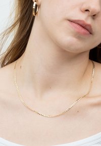 Goldkette mit flachem, strukturiertem Design und miteinander verbundenen Gliedern, die auf einem freien Hals liegt. Schlichte, elegante Ästhetik.