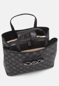 Sac fourre-tout noir à motif avec deux poignées, détail logo en métal sur le devant, et pochette intérieure zippée avec doublure beige.