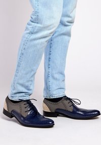 Marineblauwe leren schoenen met textuurdetails, grijze stofaccenten en een strak ontwerp. Kenmerkt zich door ronde veters en een lage hak.