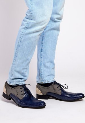 Marineblauwe leren schoenen met textuurdetails, grijze stofaccenten en een strak ontwerp. Kenmerkt zich door ronde veters en een lage hak.