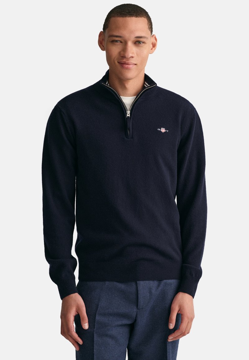 Navyblauwe zip-up trui gemaakt van zacht breimateriaal, met een hoge kraag en een klein logo op de borst. Geribde manchetten en zoom.