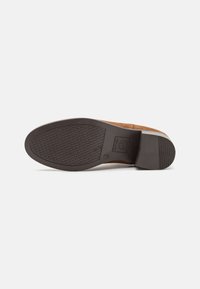 Zapato de ante marrón con una suela de goma texturizada, que presenta un ligero tacón y un perfil plano, diseñado para la durabilidad y el confort.