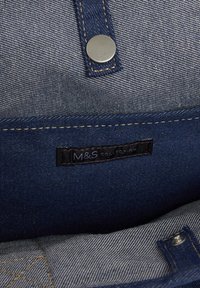 Interiér denimové tašky má modrou látku se šedým nádechem, stříbrné zacvakávací uzávěr a štítek M&S Collection. Švy jsou viditelné po celé délce.