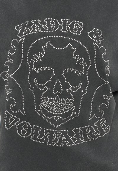 Grijze stof met een doodskopontwerp gemaakt van zilveren rhinestones, met de merknaam "ZADIG & VOLTAIRE" in een decoratieve lettertype eronder.