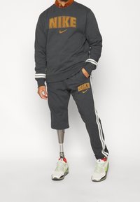 Dark gray Nike sweatshirt with large logo, paired with matching gray shorts featuring white side stripes. Worn with white and green sneakers.