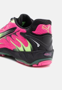 Talons de chaussure de sport rose et noir avec des motifs verts en forme de flammes, semelle amortissante noire, et un logo Puma jaune néon à l'arrière.