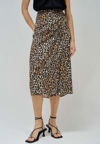 Jupe midi imprimée léopard en tissu lisse, avec un design portefeuille et une fente haute à l'ourlet ; associée à des escarpins noirs à lanières.