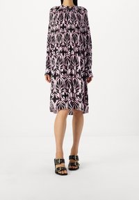 Dlouhý rukáv šatů se vzorem černých a růžových listů. Látka je měkká; střih je volný s kulatým výstřihem a nařasením.