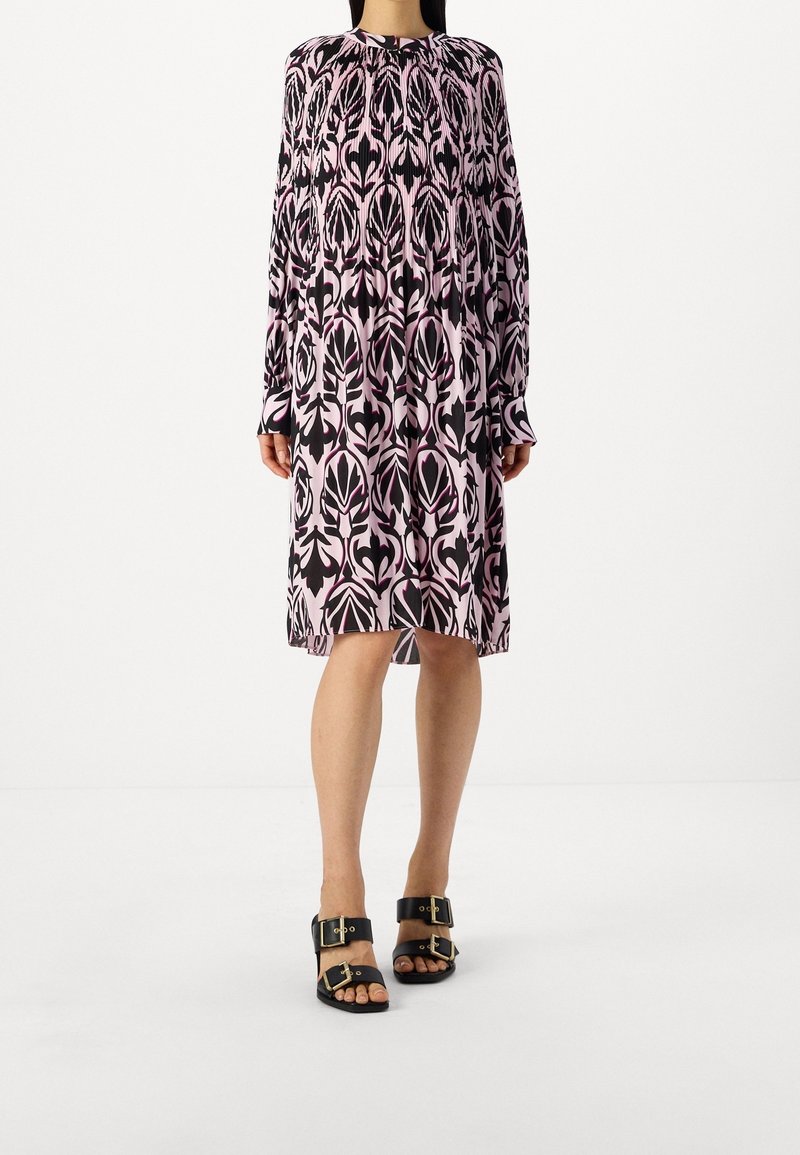 Dlouhý rukáv šatů se vzorem černých a růžových listů. Látka je měkká; střih je volný s kulatým výstřihem a nařasením.