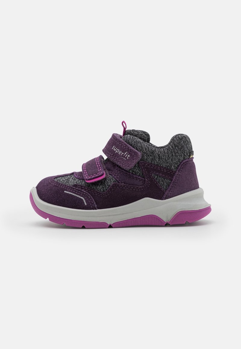 Zapatilla deportiva púrpura con un upper de tela gris, acentos de ante, tira de Velcro y suela rosa. Presenta un diseño texturizado para un agarre adicional.