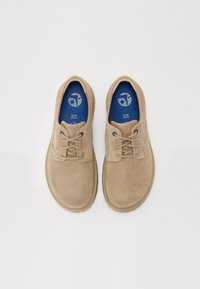 Beige semskede snøresko med rund tå, med en teksturert overflate og en blå innersåle med trykt logo. Fleksibel gummisåle.
