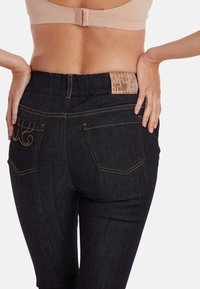 Jean en denim foncé avec une taille haute, présentant des coutures orange, deux poches arrière et une étiquette tissée au dos.