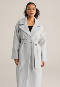 Palton lung gri deschis cu guler larg, curea frontală legată și mâneci lungi; confecționat dintr-un material moale și texturat. Are buzunare laterale.