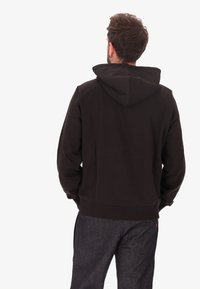 Felpa nera con cappuccio regolabile e vestibilità comoda, abbinata a pantaloni in denim scuro, mostrano una texture morbida e un design semplice.