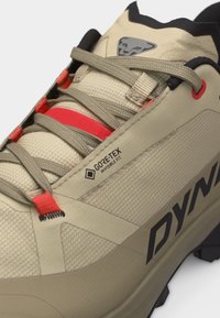 Beżowo-czerwony but turystyczny Dynafit z etykietą Gore-Tex Invisible Fit, wzorzystą tkaniną i widocznym czarnym bieżnikiem podeszwy.