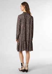 Braunes Kleid mit einem quadratischen Muster in hellem Beige. Verfügt über lange Ärmel, einen gerafften Ausschnitt und einen gestuften, gerüschten Saum. Kombiniert mit beigen Ankle Boots.