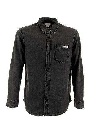 Camisa de mezclilla negra con mangas largas, cierre de botones en la parte frontal y un único bolsillo en el pecho con una etiqueta de logo. Diseño clásico de cuello.
