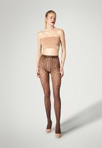Leggings transparents marron avec un motif de dentelle élaboré, dotés d'une taille haute et associés à un bandeau ajusté nude et des talons nude.