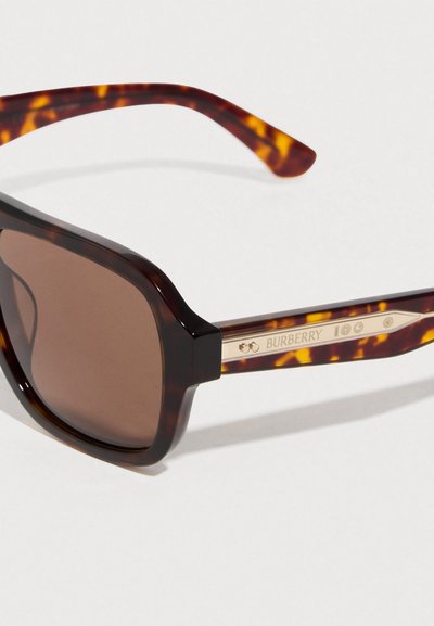Γυαλιά ηλίου με κορνίζα τύπου χελώνας, παχιές, με καφέ βαθμιαία σκουρότερους φακούς και εξαρτήματα σε χρυσό χρώμα που φέρουν το λογότυπο της Burberry στο πλευρό.