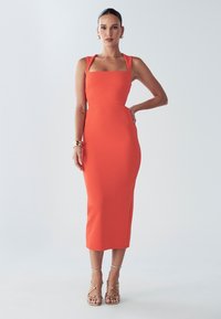 Figursyet knælang kjole i lyst orange stof. Har firkantet udskæring, brede stropper og glat tekstur. Letvægts, elegant design.