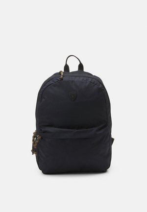 Sac à dos Polo noir avec poche zippée avant, poignée supérieure et tirettes de fermeture éclair tressées, présenté sur un fond clair uni.